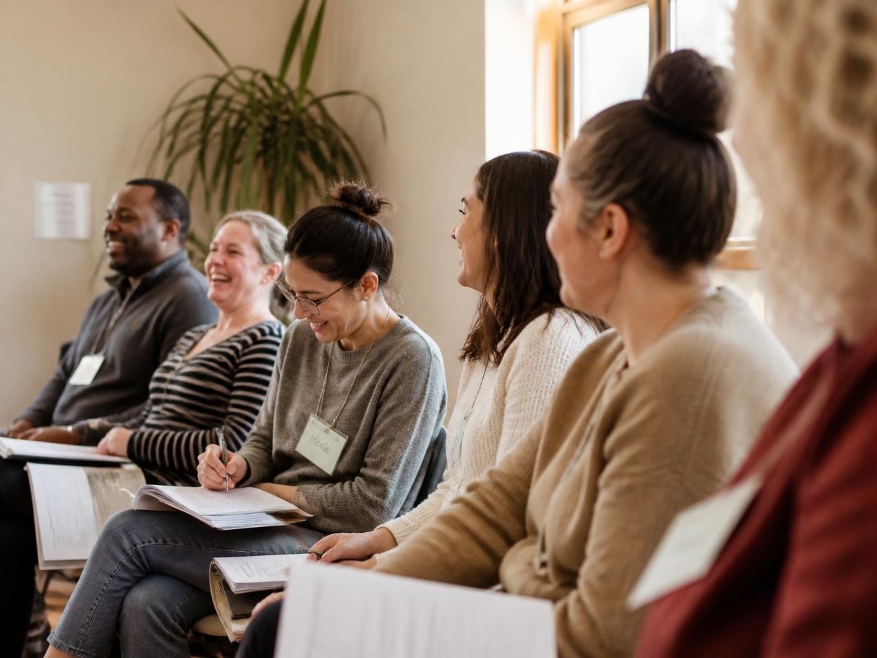 A diverse group of early childhood educators seated together, taking notes and laughing during a storytelling professional development workshop